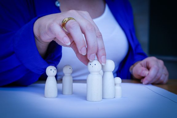 Eine Hand platziert eine Figur auf einer Gruppe von Holzfiguren auf einem Tisch.